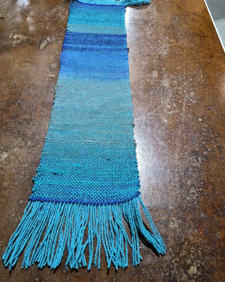 A handwoven sample shading from royal blue into bright turquoise, finished with a thick turquoise fringe.