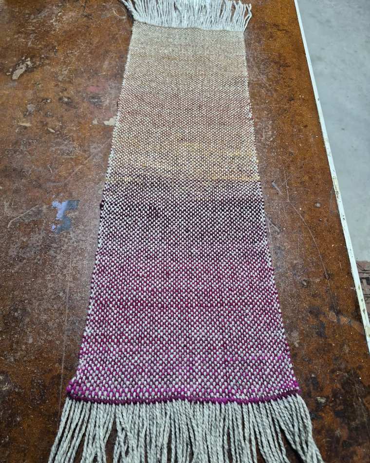 A handwoven sample shading from soft cream through dusky mauve into bright magenta, with a pale grey fringe.