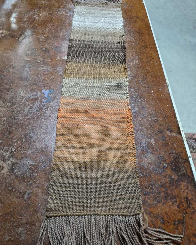 A handwoven sample in bands of cream, dark brown and soft orange, settling into warm tan, with a light brown fringe.