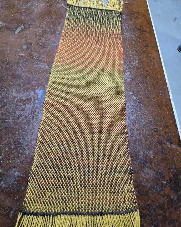 A handwoven sample shading from rust and orange through olive into golden yellow, with a yellow fringe.