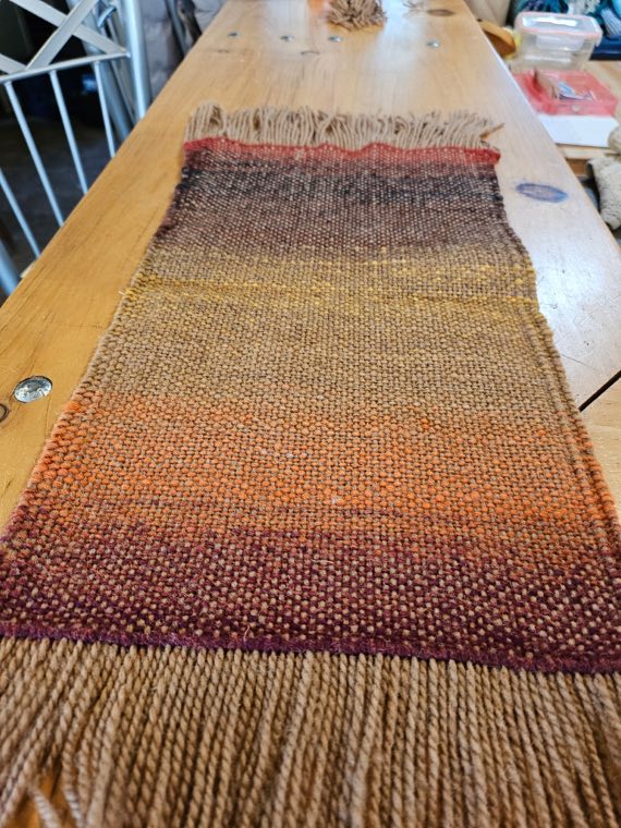 A handwoven sample in rust, gold and deep burgundy stripes with a long sandy fringe.
