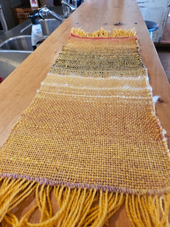 A handwoven sample in warm golds and ochres with a pale cream band woven across the middle.