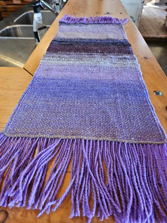 A handwoven sample shading through lavender and soft grey, finished with a deep purple fringe.